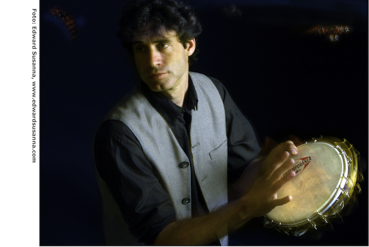 Michael de Miranda playing a pandeiro in warm stage light